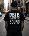 Person wearing a black t-shirt with 'Dust is part of the sound' text on a city street.