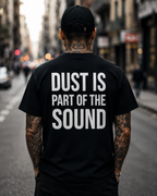 Person wearing a black t-shirt with 'Dust is part of the sound' text on a city street.